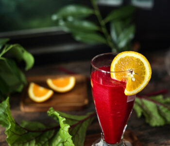 Smoothie z buraków i pomarańczy w szklance na drewnianym blacie, obok świeże buraki i pomarańcze