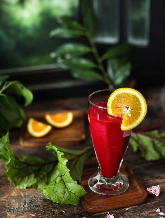Smoothie z buraków i pomarańczy w szklance na drewnianym blacie, obok świeże buraki i pomarańcze