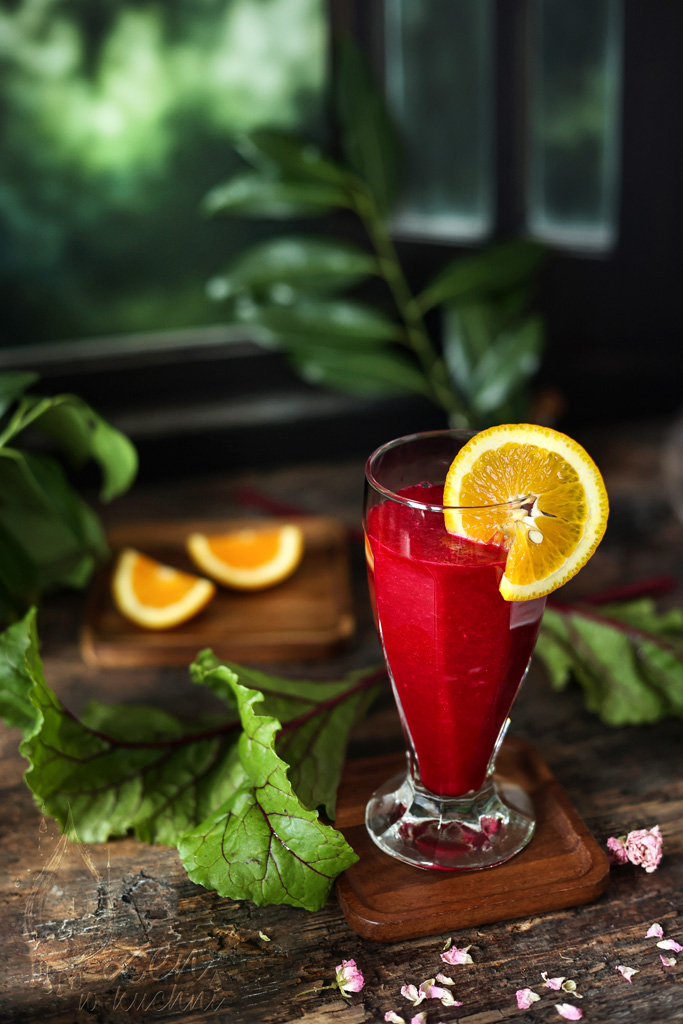 Smoothie z buraków i pomarańczy w szklance na drewnianym blacie, obok świeże buraki i pomarańcze